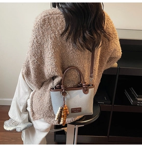 Detail of grey canvas bucket bag with brown leather trim and colorful beaded tassel charm