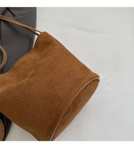 Détail du sac seau en daim marron montrant la texture douce et les bords passepoilés