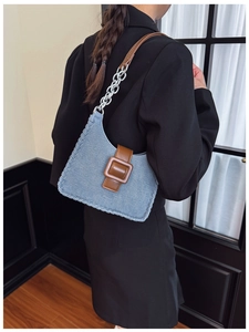 Détail du sac à bandoulière en denim bleu clair avec lanière en cuir brun et chaîne