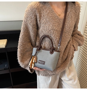 Detail of grey canvas bucket bag with brown leather straps and wooden bead charm on a model