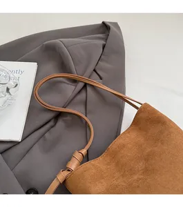 Détail du sac seau en daim marron avec fine bandoulière en cuir nouée élégante