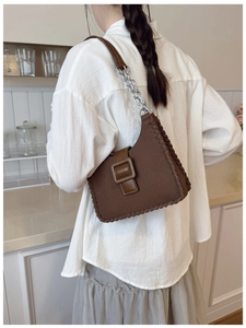Détail d'un sac porté épaule marron avec bords tressés, grande boucle et chaîne argentée