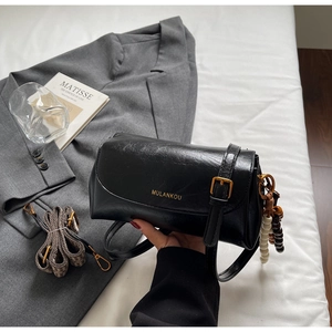 Détail du sac à bandoulière en cuir noir avec boucle dorée et breloque perlée