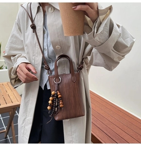 Close-up of brown woven mini crossbody bag with bohemian style wooden bead tassel detail