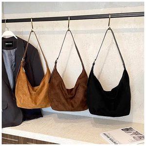 Three suede hobo shoulder bags in camel, brown, and black hanging on a metal rack