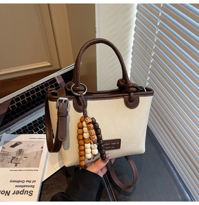 Detail of canvas tote bag featuring premium leather handles and a wooden bead charm