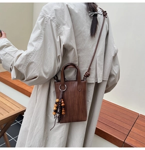 Detail of a brown woven mini crossbody bag with a decorative wooden bead tassel pendant