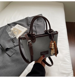 Detail of grey canvas bucket bag with brown strap and colorful wooden bead tassel charm