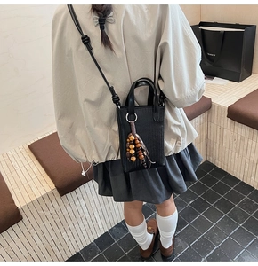 Detail of black woven mini crossbody bag with wooden bead tassel on a model
