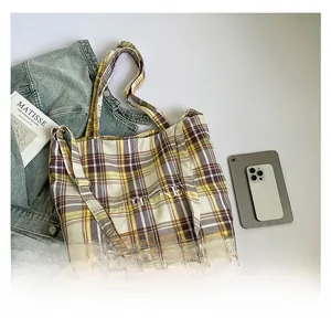 Flat lay of plaid tote bag with TESHONE lettering, denim jacket, and daily accessories