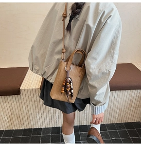 Detail of a brown woven texture mini crossbody bag featuring a retro wooden bead tassel charm