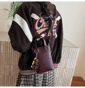Detail view of burgundy crossbody bag with woven texture and decorative wooden bead charm