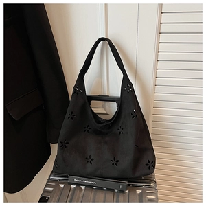 Vue détaillée du sac hobo en daim noir avec motifs floraux découpés sur une valise