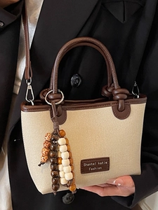 Minimalist canvas bucket bag with brown leather trim and beaded tassel in a front view