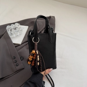 Detail of black woven texture bag featuring vintage wooden bead tassel and slim strap