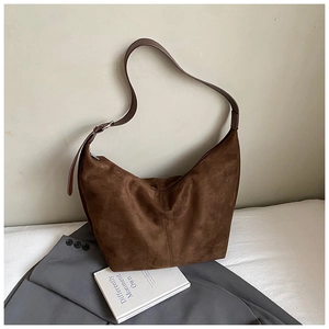 Detail of a brown suede hobo bag with adjustable strap on a white sofa setting