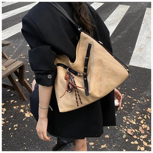 Close-up of a camel suede tote bag with contrast black straps and side buckle details