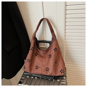 Détails des motifs de fleurs découpés au laser sur un sac cabas en daim marron foncé
