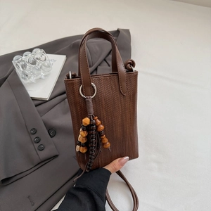 Macro detail of brown woven texture mini crossbody bag with wooden bead tassel charm