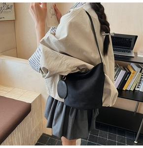 Détail d'un sac seau en cuir noir mat avec un porte-monnaie rond sur la bandoulière