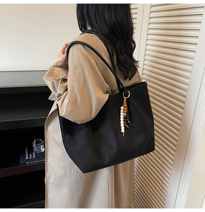 Detail einer schwarzen Shopper-Tasche mit Perlenanhänger, über der Schulter getragen