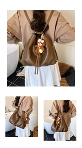 Detail of dark brown leather tote bag with plush bear charm and dual-strap backpack styling