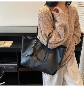 Detail of black tote bag with small round coin purse and textured leather on a model