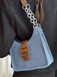 Sac sous le bras en denim bleu avec bandoulière en cuir marron sur un blazer de couleur sombre