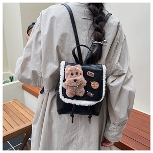 Mini black and white leather backpack with plush dog charm worn over a beige coat