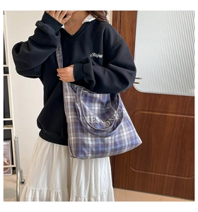 Model wearing a large purple and blue plaid tote bag in a minimalist indoor setting