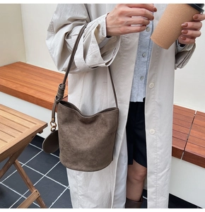 Détail du sac seau en daim marron foncé avec bandoulière réglable et charme décoratif