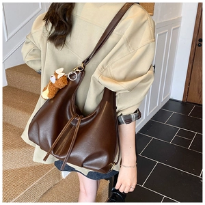 Detail of dark brown leather hobo bag featuring a plush dog charm and crossbody strap