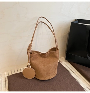 Détail du sac seau en daim avec poignée en cuir et pendentif porte-monnaie rond