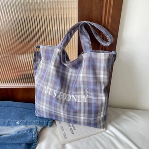 Detail of purple plaid canvas tote bag with embroidered YES HONEY text and smile icon