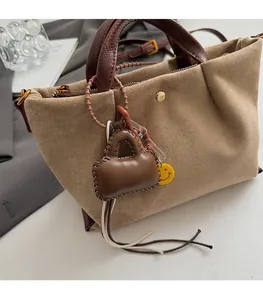 Détail du sac seau en daim avec poignées en cuir et breloque décorative smiley