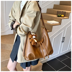 Brown faux leather hobo tote bag worn with trench coat, featuring a cute teddy bear charm