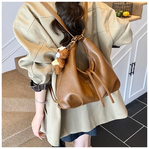 Side view of a vintage caramel brown tote bag with a cute plush bear charm on soft leather
