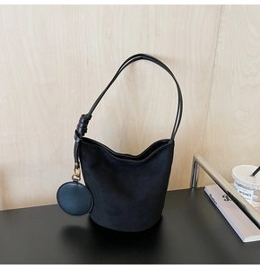 Détail du sac seau noir en daim avec fines bretelles nouées et petit charme assorti