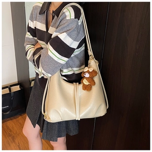 Cream tote bag with a cute brown plush bear charm worn by a model in a natural setting