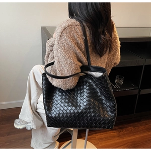 Close-up of a large black woven leather tote bag shown on a person shoulder