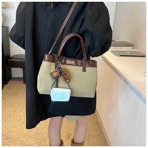 Detail view of khaki canvas handbag with brown leather straps and decorative hanging charms