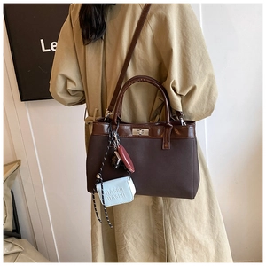Deep brown tote bag with silver lock and charms styled on a trench coat for chic daily commute