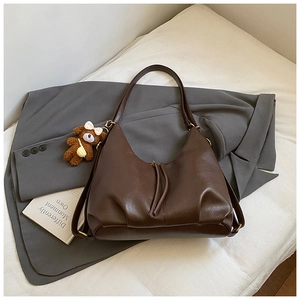 Detail of dark brown faux leather tote bag with plush bear charm on a grey blazer