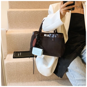 Detail view of dark brown paneled handbag with light blue charm shown with white blazer