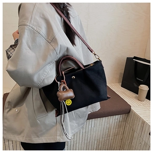 Détail d'un sac cabas en toile noire avec poignées en cuir et charm pelucheux mignon