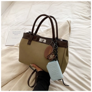 Detail of khaki tote bag featuring blue charm accessories and brown leather handles