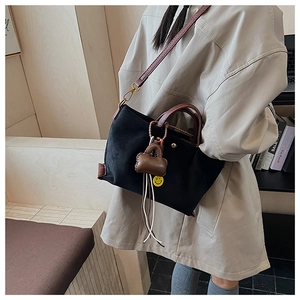 Détail d'un sac cabas noir minimaliste avec anses marron vintage et badge sourire jaune