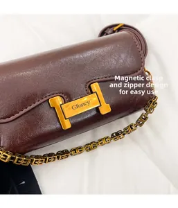 Gros plan d'une boucle magnétique dorée en H sur un sac à main en cuir marron brillant