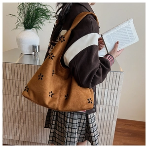 Detail of brown suede tote with laser-cut flower patterns and wide shoulder strap