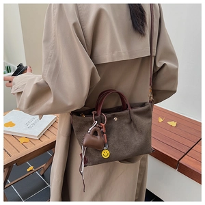 Détail d'un sac cabas en daim marron avec poignées rouges et breloques colorées sur l'épaule